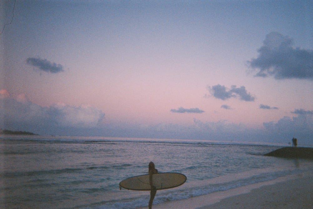 Surfer silhouetted against a pink sunset sky