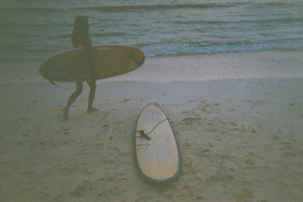 Two surfboards resting on white sand at the shoreline