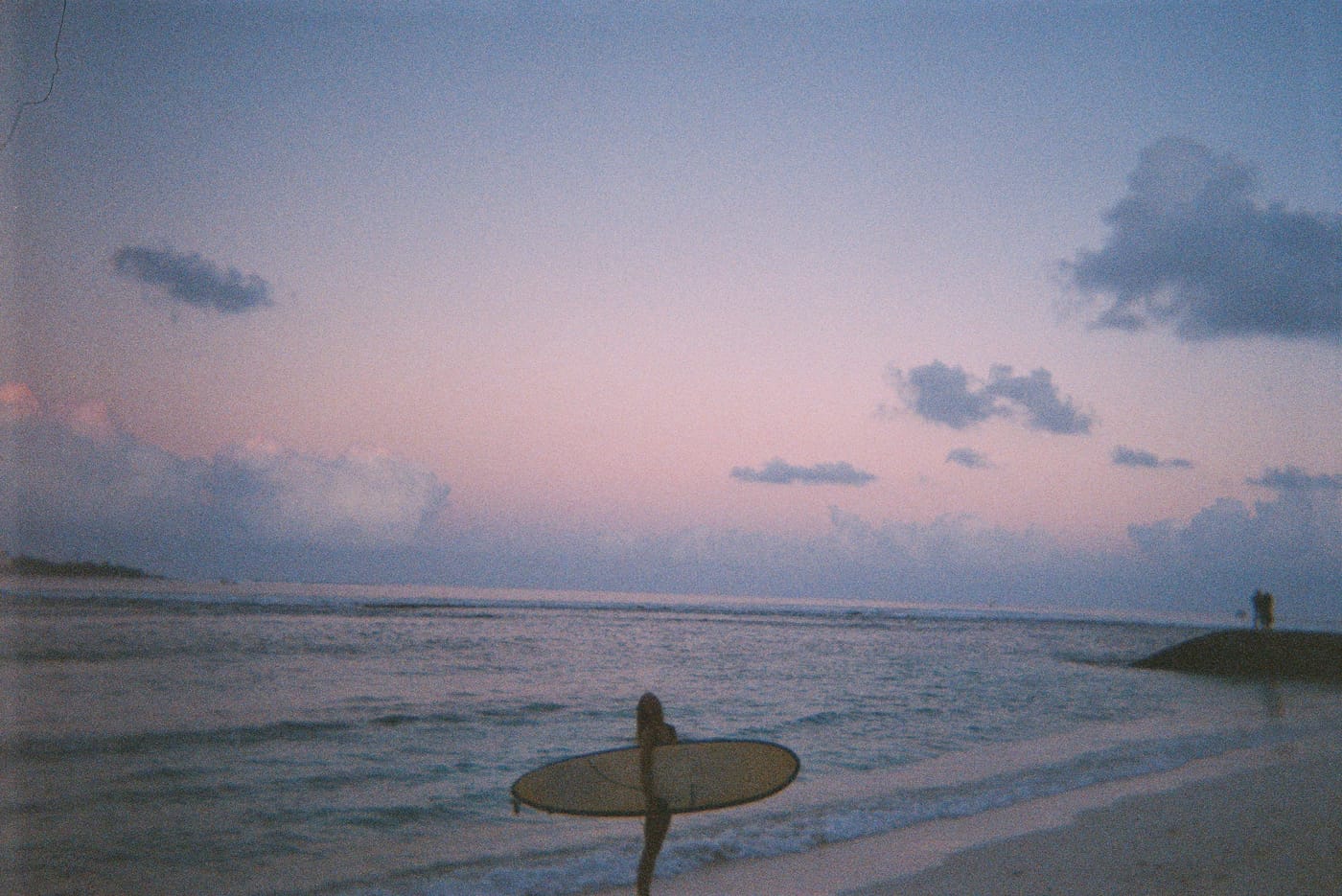 Surfer carrying a board at sunset on a Maldives beach